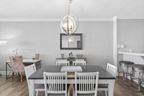 A dining area with a rectangular table, white chairs, a chandelier, and a mirror on the wall. - Ocean Reef (Panama City Beach)