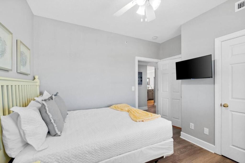 A bedroom with a bed, a ceiling fan, a television on the wall, and a door.