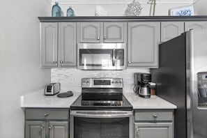 A kitchen with grey cabinets, a stainless steel refrigerator, a microwave, a stove, and a toaster. - Ocean Reef (Panama City Beach)