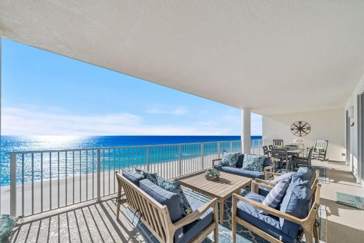 A balcony with a view of the ocean, furnished with a table and chairs, and a compass wall decoration.