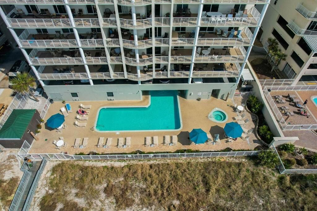Un hotel de varios pisos con una zona de piscina en la azotea, que incluye tumbonas y sombrillas.