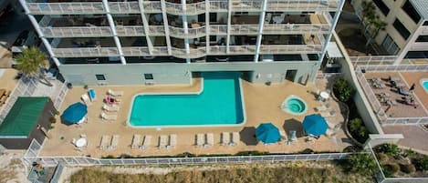 Un hotel de varios pisos con una zona de piscina en la azotea, que incluye tumbonas y sombrillas.