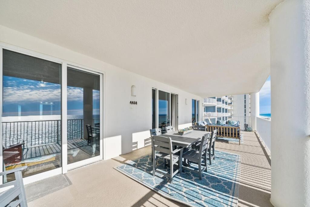 A balcony with a dining table and chairs, a view of the sea, and a building with balconies.