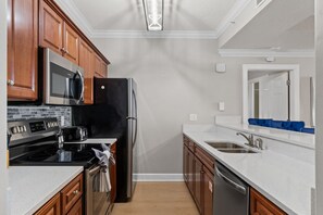 A modern kitchen with wooden cabinets, a black refrigerator, stainless steel appliances, and a white countertop. - Ocean Ritz (Panama City Beach)