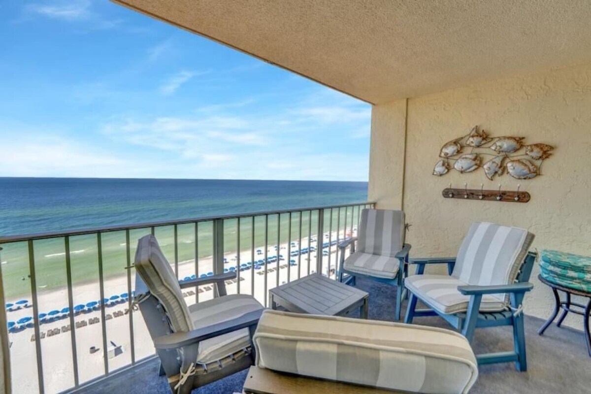 A balcony with a view of the ocean, featuring striped chairs and a small table.