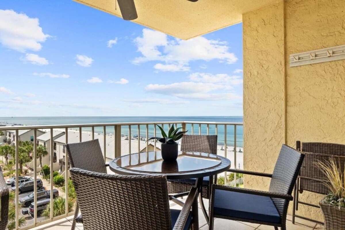 A balcony with a round table and wicker chairs, overlooking a beach.
