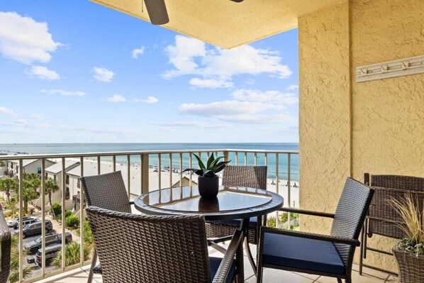 A balcony with a round table and wicker chairs, overlooking a beach. - Regency Towers (Panama City Beach)
