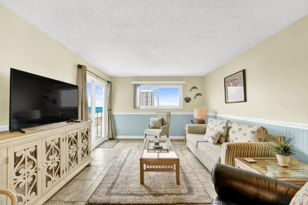 A living room with a flat-screen TV, a sofa, a coffee table, and a window with a view of a building.