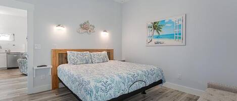 A bedroom with a bed, a painting of a beach scene, and a wooden headboard.