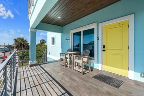 Ein Balkon mit Holzboden, einer gelben Tür und einem Tisch mit Stühlen.