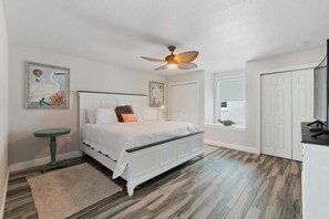 A bedroom with a bed, a ceiling fan, a green side table, and artwork on the walls. - Sandy Toes (Flagler Beach)
