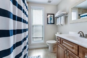 A bathroom with a striped shower curtain, a toilet, a sink with a mirror, and a framed seahorse artwork on the wall. - Sandy Toes (Flagler Beach)