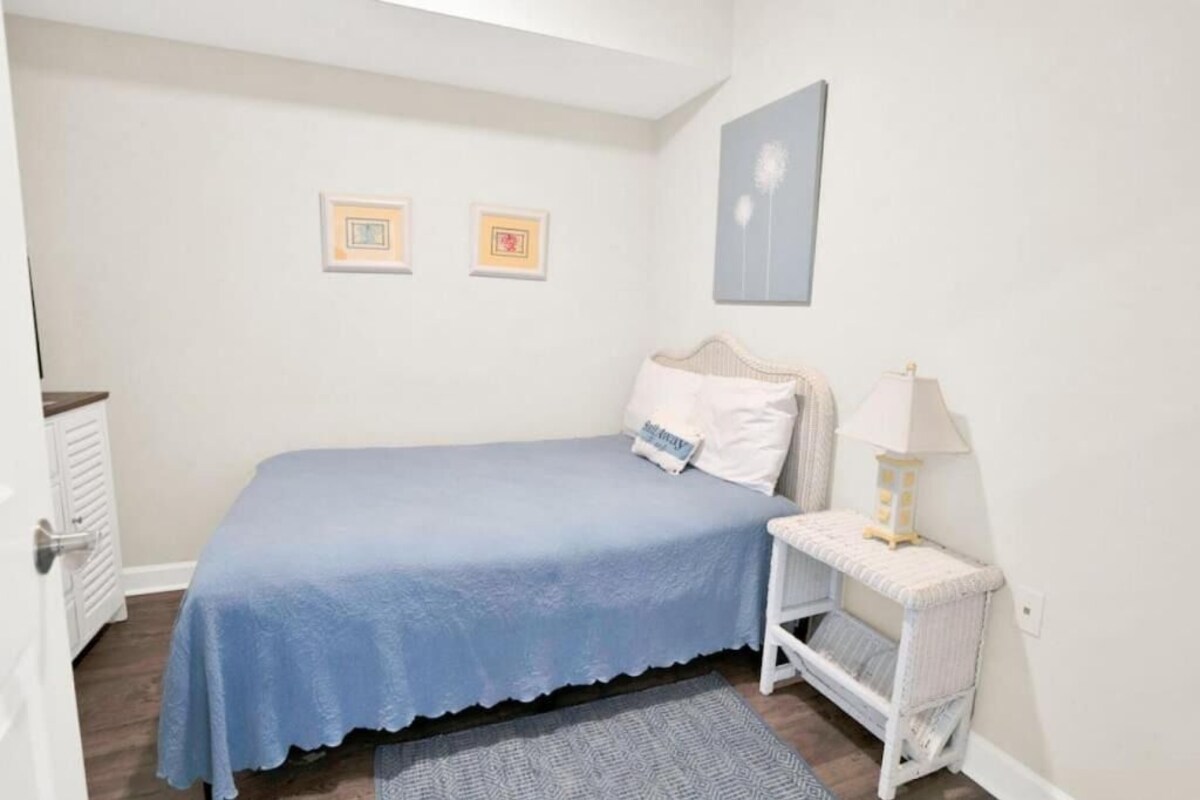 Ein Schlafzimmer mit einem Bett, einem Nachttisch mit Lampe und zwei gerahmten Bildern an der Wand.