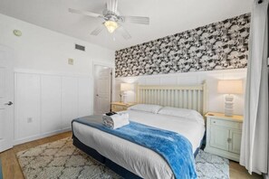 Ein Hotelzimmer mit Bett, Deckenventilator, Heizkörper, Nachttisch und einer Wand mit floralem Muster.