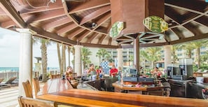 An outdoor bar area with wooden tables and chairs, a counter with a cash register, and a view of the ocean. - Shores Of Panama (Panama City Beach)