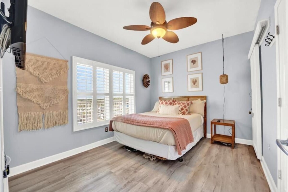 A bedroom with a bed, a ceiling fan, a window with blinds, and a wall-mounted shelf.