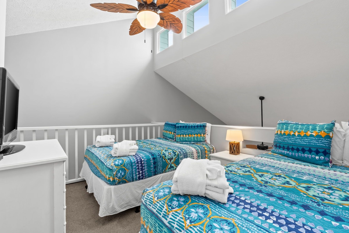Ein Schlafzimmer mit zwei Betten, einem Schreibtisch und einem Deckenventilator.