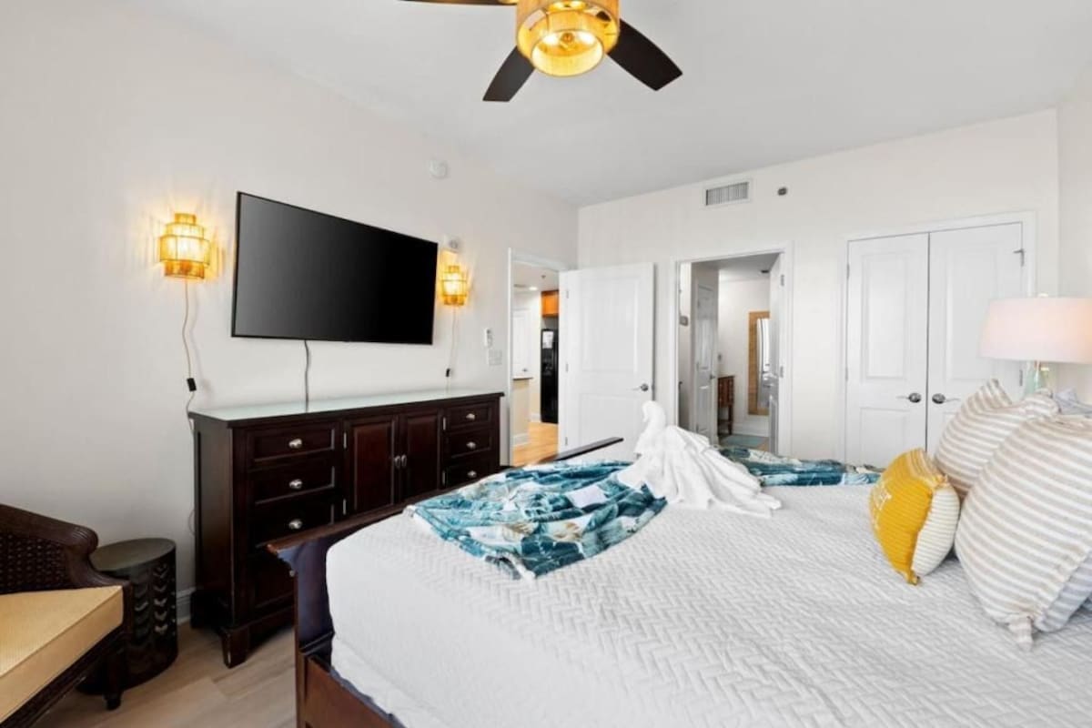 A hotel room with a bed, a flat-screen TV, a ceiling fan, and a nightstand.