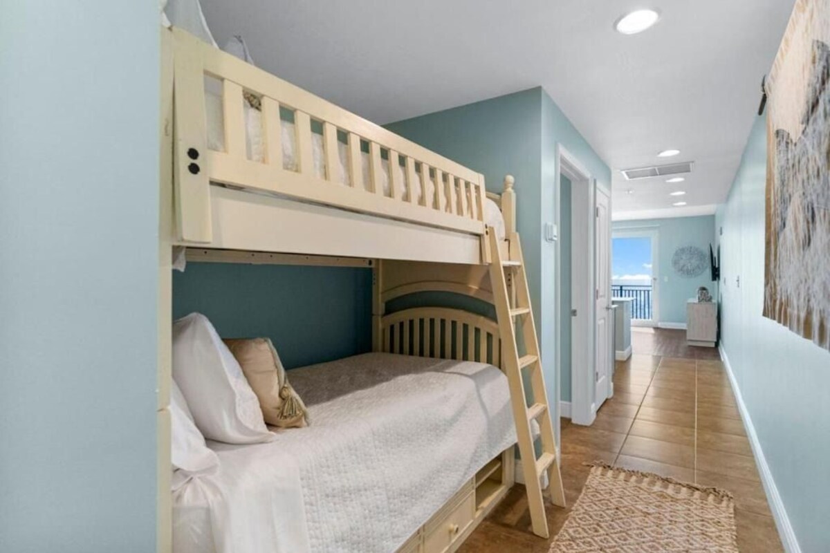 A bunk bed in a room with a view of the sea through a door.