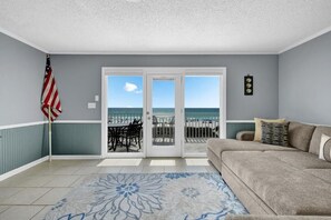 A room with a view of the beach, a couch, a patterned rug, and an American flag. - Surf Club (Panama City Beach)