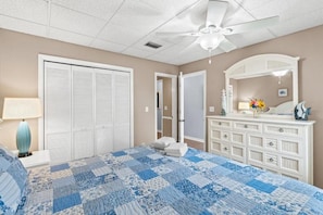 A bedroom with a bed, a dresser, a mirror, and a ceiling fan. - Surf Club (Panama City Beach)