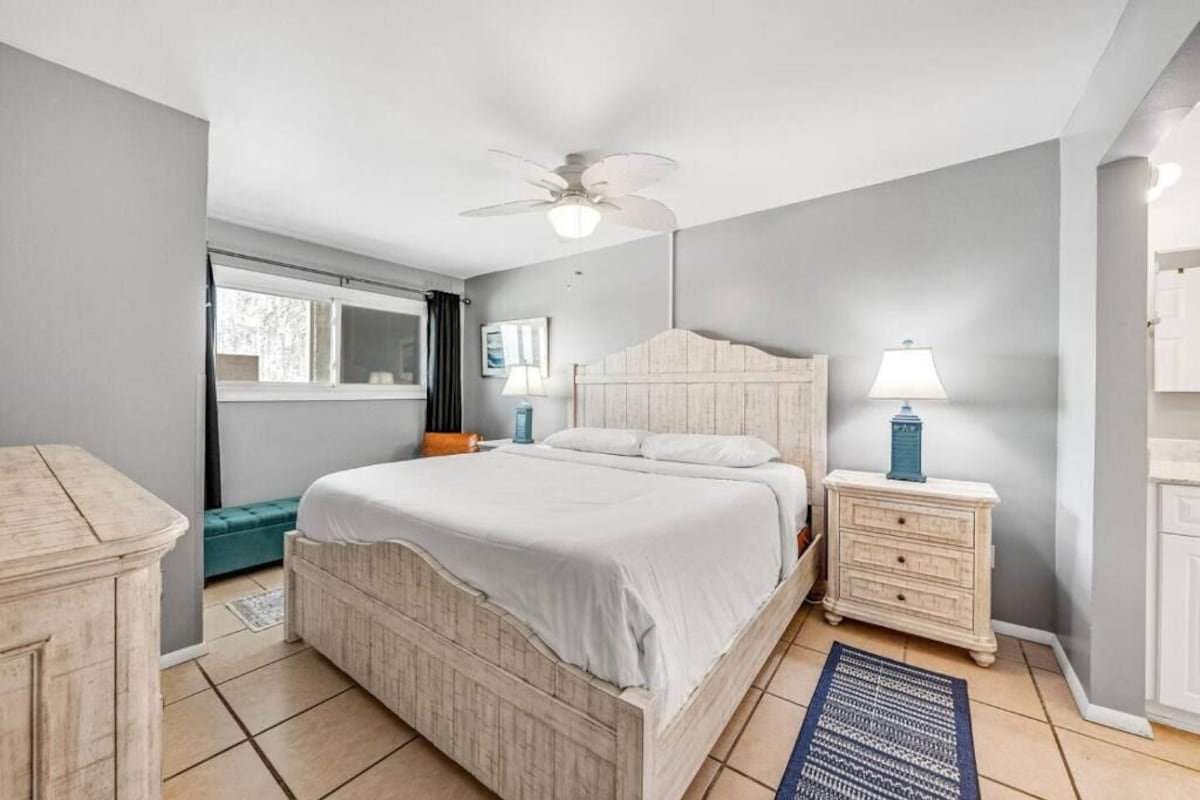 A bedroom with a bed, nightstands, a lamp, a ceiling fan, and a window.