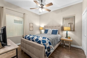 A bedroom with a bed, bedside lamps, a ceiling fan, a TV, and a window with blinds. - Tidewater (Panama City Beach)
