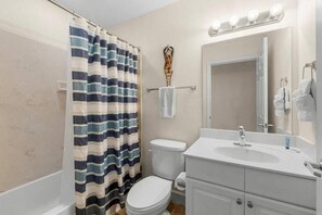A bathroom with a striped shower curtain, a toilet, a sink with a mirror, and a towel rack. - Tidewater (Panama City Beach)