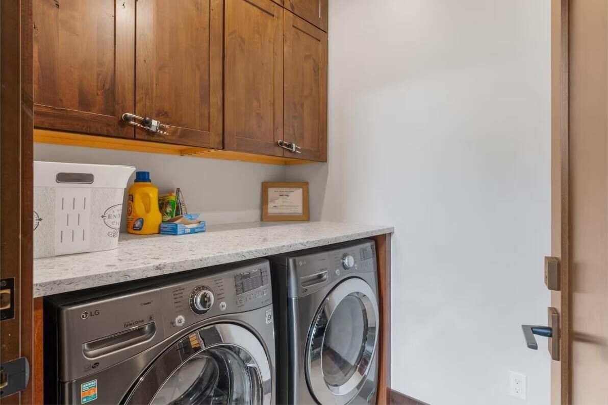 A laundry area with two front-loading washing machines, wooden cabinets above, and a countertop with cleaning supplies.