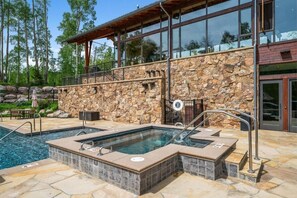 Een zwembadgedeelte met een stenen muur, een hottub en een houten terras.
