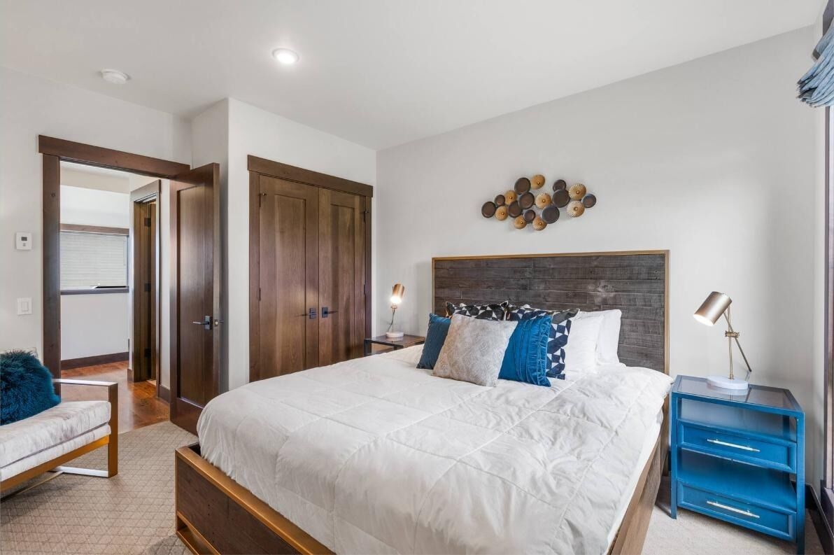 A bedroom with a large bed, a wooden headboard, a nightstand with a lamp, and a wall-mounted decoration.