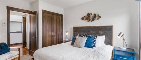 A bedroom with a large bed, a wooden headboard, a nightstand with a lamp, and a wall-mounted decoration.