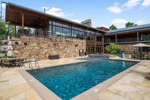 Ein Schwimmbad mit Steinplatten, einer überdachten Terrasse und einem Gebäude mit großen Fenstern.