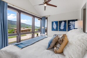 Een slaapkamer met een groot bed, een plafondventilator en uitzicht op de omgeving.