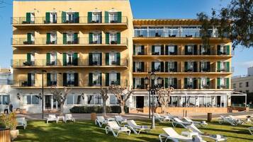 Un hotel de varios pisos con balcones, mobiliario exterior y un césped bien cuidado.