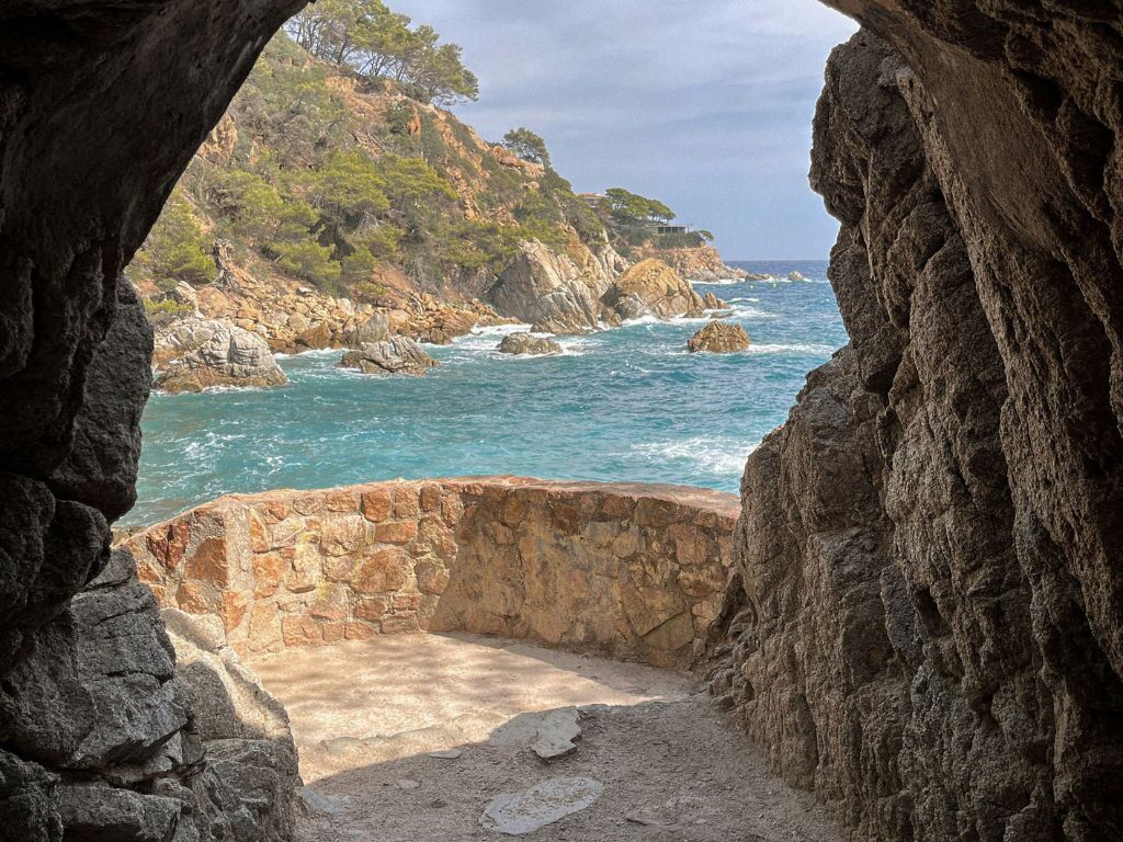 Une vue sur la côte, encadrée par une arche rocheuse, avec un sentier de pierres menant à la mer.