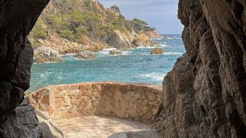 Une vue sur la côte, encadrée par une arche rocheuse, avec un sentier de pierres menant à la mer.
