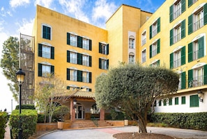A yellow building with green shutters, a staircase, and a tree in the foreground.