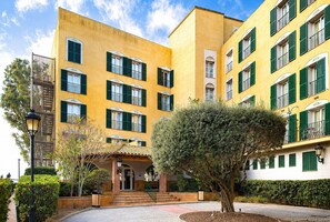 A yellow building with green shutters, a staircase, and a tree in the foreground.