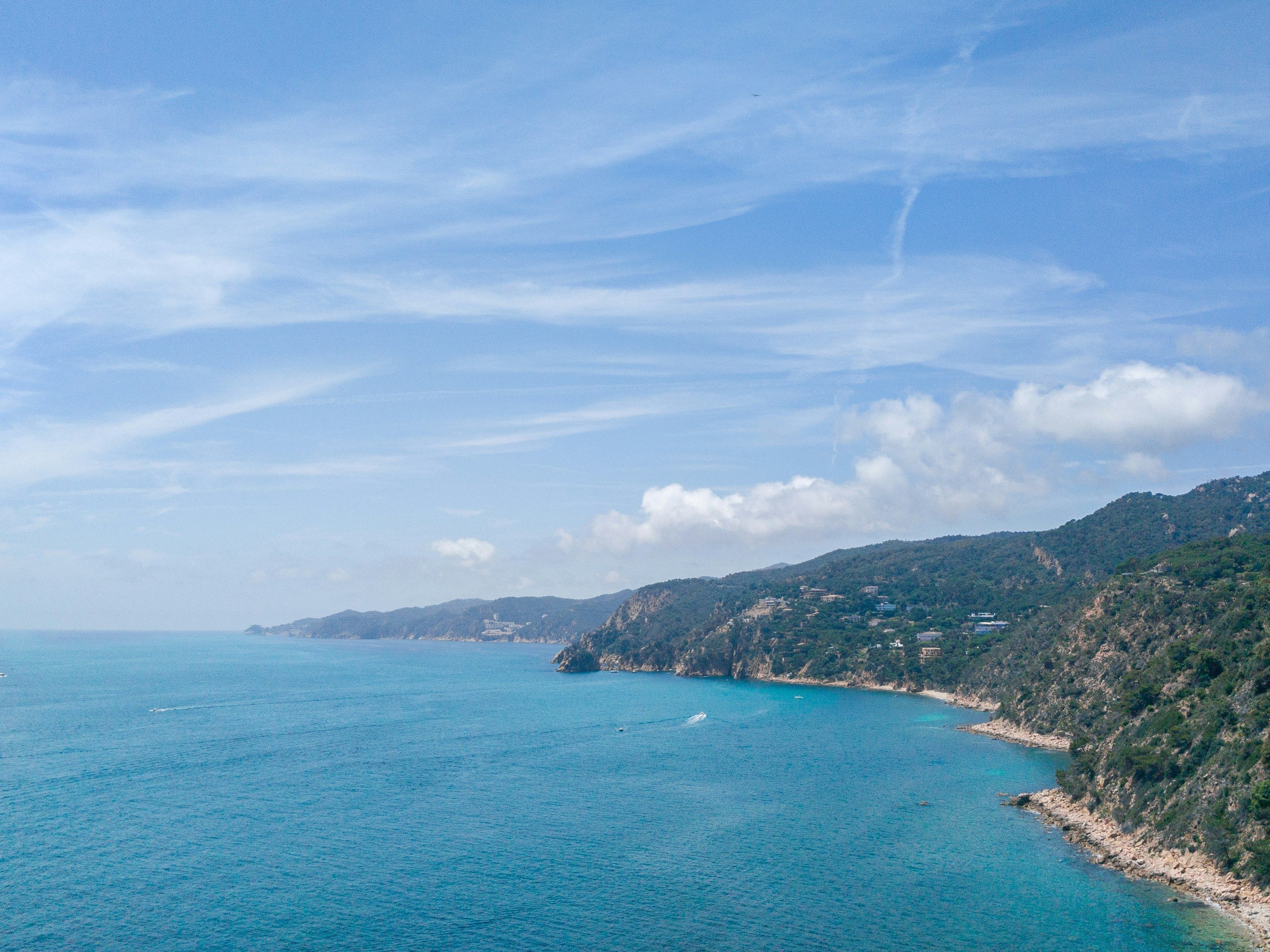 Eine Küstenlandschaft mit blauem Himmel, ruhiger See und hügeligem Gelände mit Gebäuden.