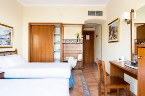 A hotel room with two beds, a desk, a chair, a small table, and a bathroom with a shower and toilet.