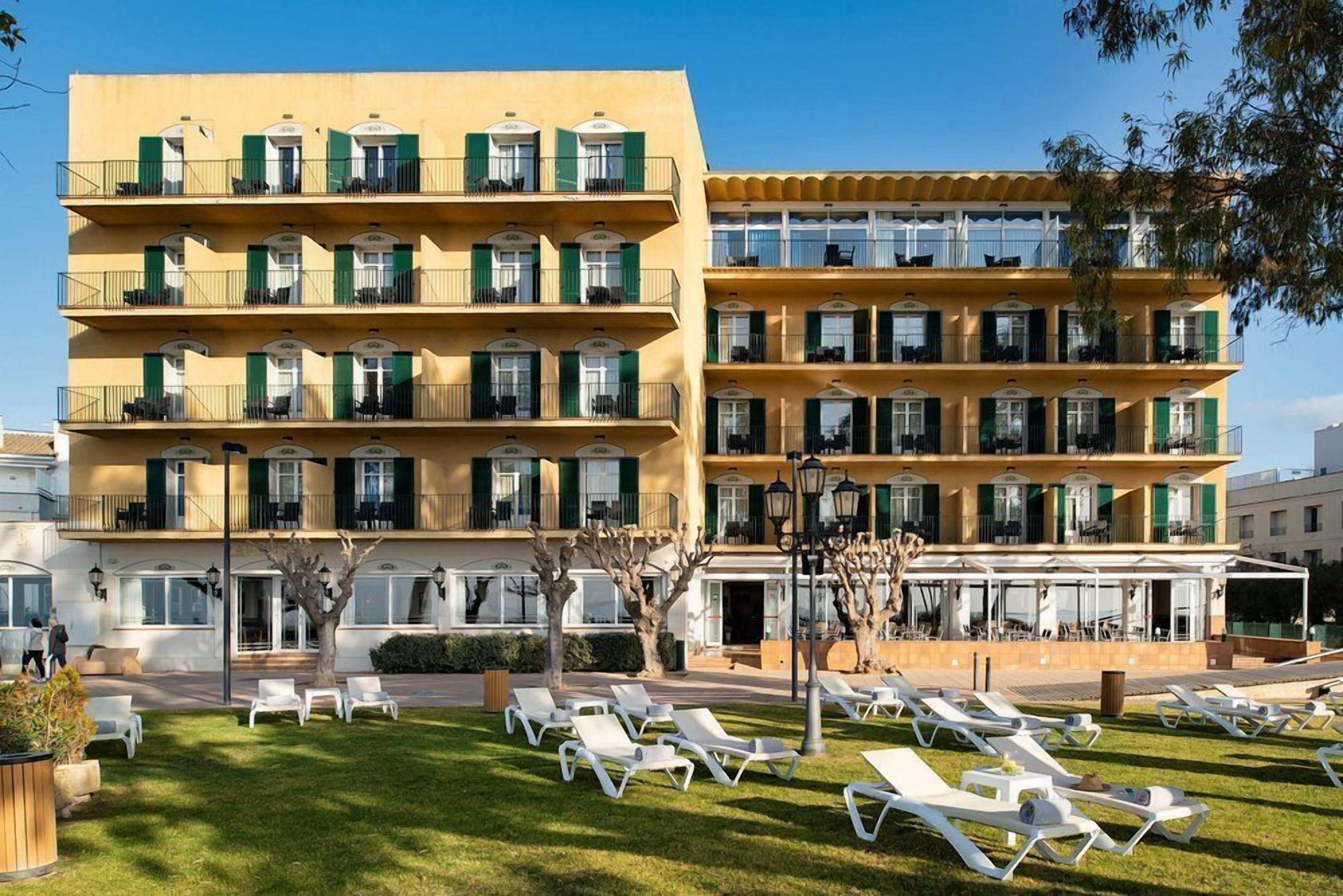 Een hotel met meerdere verdiepingen, balkons, terraszitplaatsen en een verzorgd gazon.