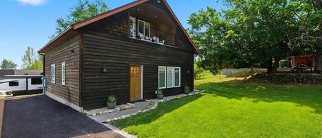 A two-story log cabin with a front porch, a covered deck, and a well-maintained lawn.