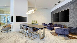 A modern interior with a central dining table, seating area with sofas, and large wall-mounted TVs.