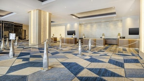 A hotel lobby with a geometric patterned carpet, a reception desk, and a large pillar.
