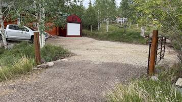 A gravel driveway leading to a red barn with a closed garage door, surrounded by trees and a parked vehicle.