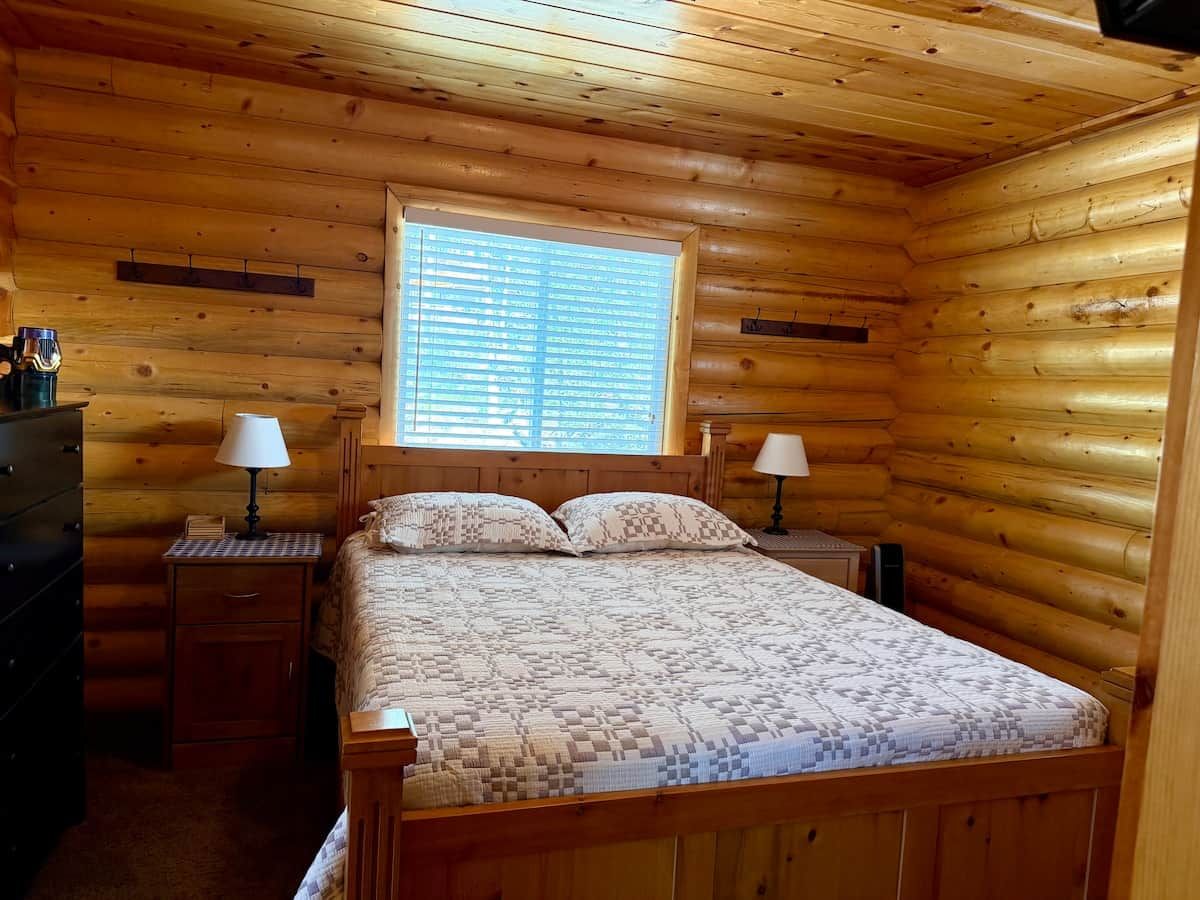 Une chambre à coucher dans une cabane en bois, avec un lit, deux tables de chevet et une fenêtre.