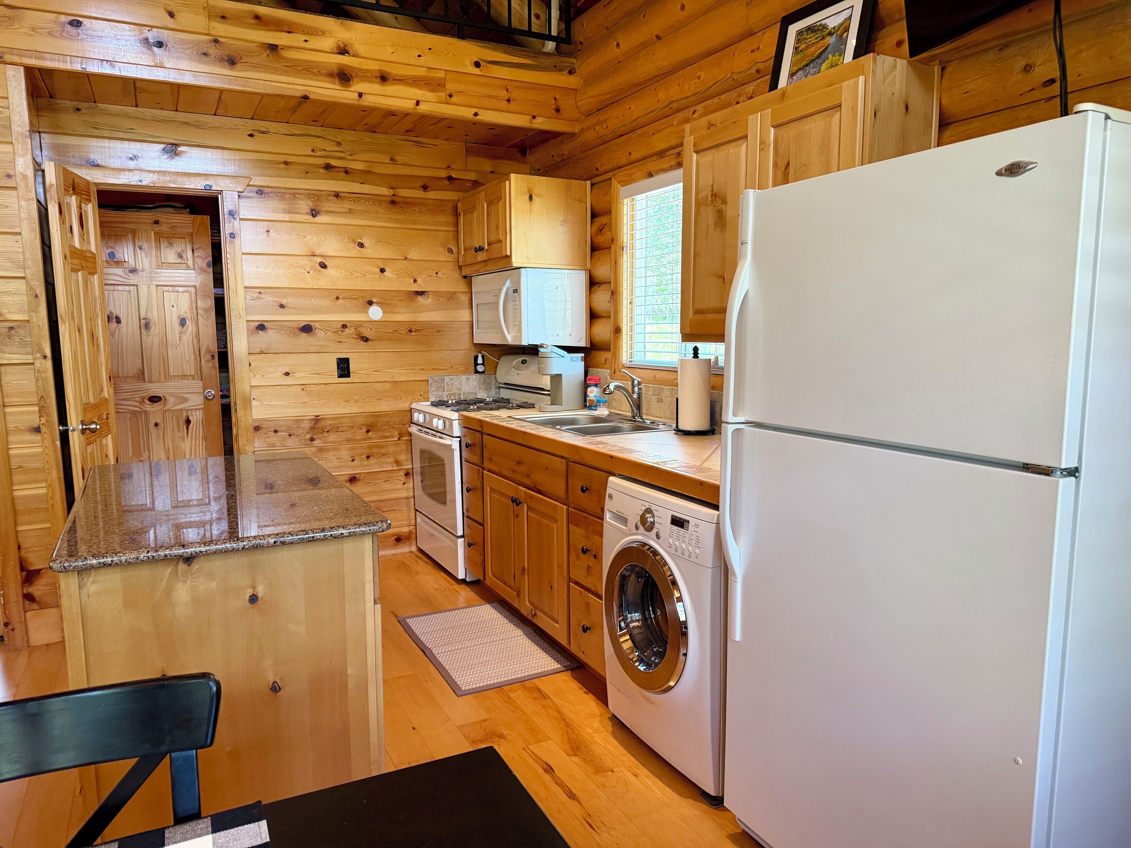 A compact kitchen with wooden walls, a built-in oven, a microwave, a washing machine, and a refrigerator.
