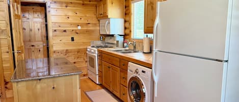A compact kitchen with wooden walls, a built-in oven, a microwave, a washing machine, and a refrigerator.