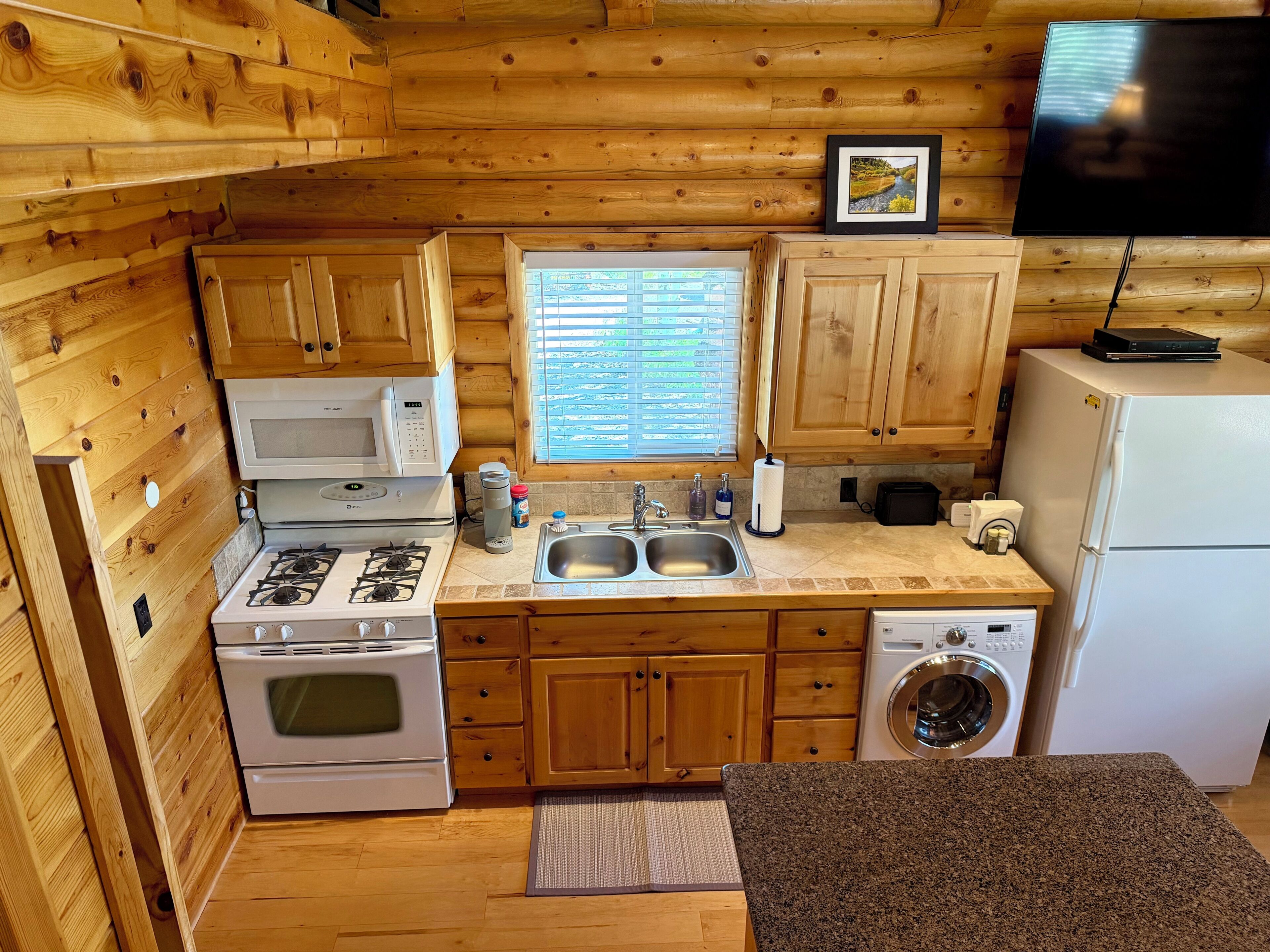 A compact kitchen with wooden cabinets, a microwave, stove, sink, and a washing machine.